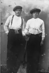Studioportrett av to brødre, fotografert stående med en spad