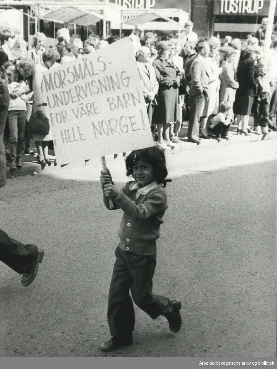1. mai 1980, Oslo. Plakat: Morsmålsundervisning for barn i hele Norge! Tekst på avisutklipp på baksiden av foto: fremmedarbeiderne utgjør et stadig viktigere element i 1. mai-feiringen.