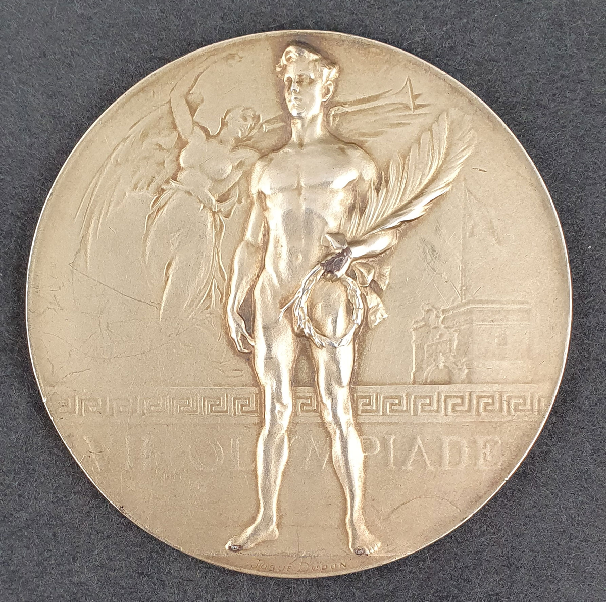 Gullmedalje fra Antwerpen 1920. På den ene siden vises en seirende atlet med krans og palmeblad i hånden. På den andre siden vises Brabo-monumentet i Antwerpen i forgrunnen og havnen i bakgrunnen.