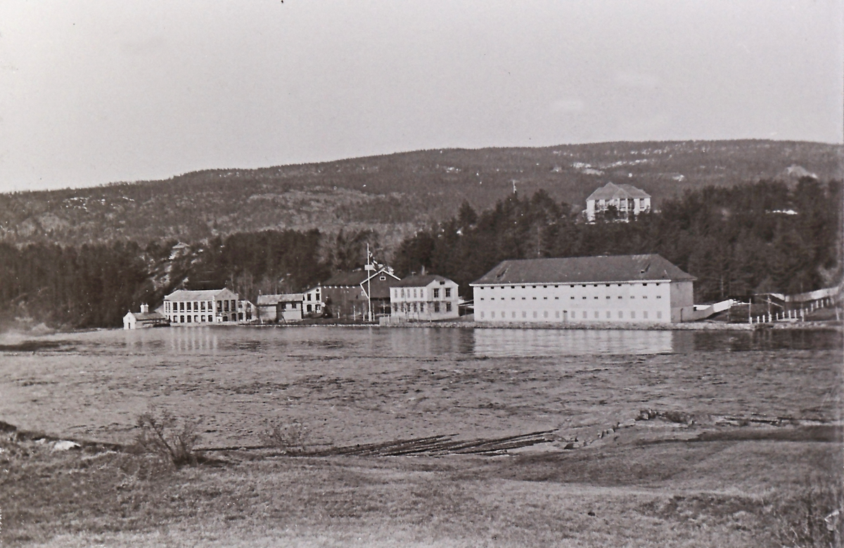 Bygningene ved "Fabrikken" set fra østsida av elva.
Bildet er tatt etter 1902, da Direktørboligen ble oppført, men før 1915, siden mitraliøseverkstedet ikke er oppført.