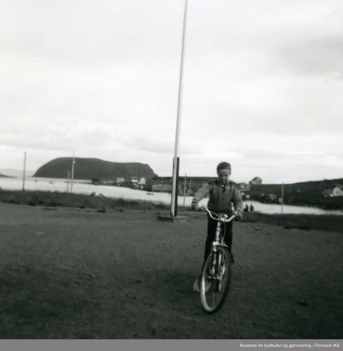 Sarnes. Rolf Ivar Iversen, elev på Solvang internatet, på sykkelen til Jan Daniel Johansen. Deler av bebyggelsen i bakgrunnen. 1963-1970.