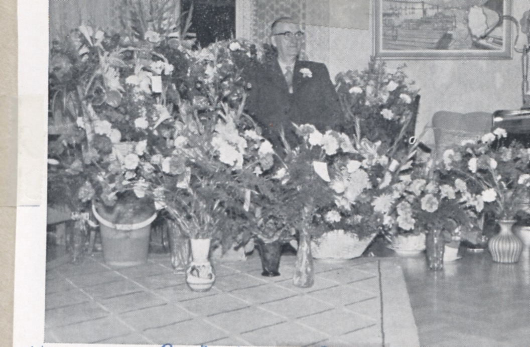 Uppvaktning av lantbrukaren Birger Pettersson (1891 - 1970), Backen eller Högen okänt årtal. Birger sitter i en stol. Framför honom finns ett bord som är fullt av blommor.