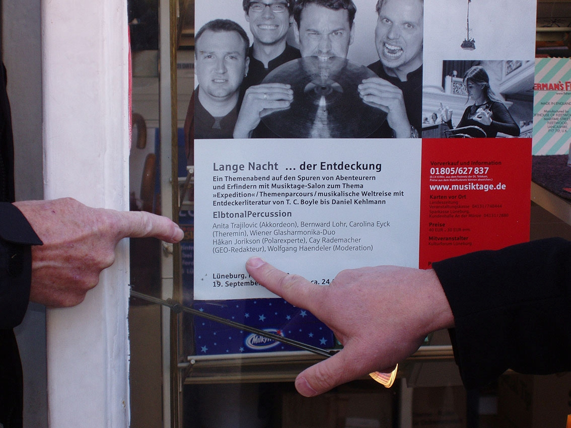 Två personer pekar på en liten affisch som sitter på ett fönster: "Lange Nacht ... Der Entdeckung", ett program som avser Niedersächsiche Musiktage i Lüneburg, Tyskland.