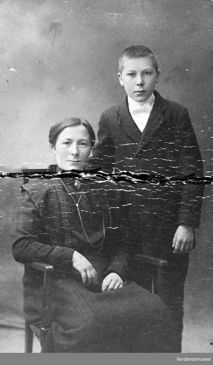 Portrett av Ella Hansen og hennes sønn Johan Olsen. dame sitter,brystnål i halsen,langt halskj. glatt hår.gutt står