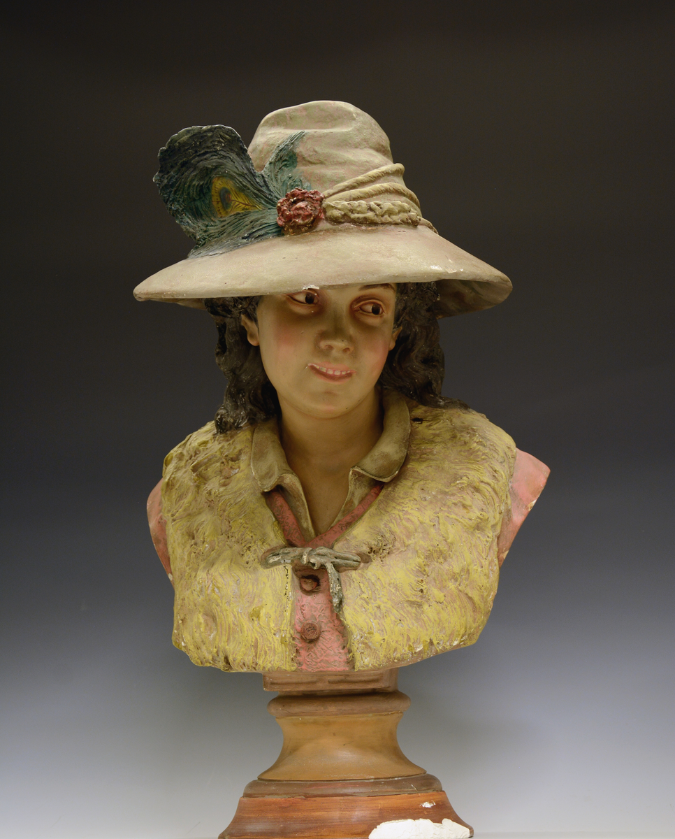 Kvinne med bredbremmet hatt, påfuglfjær og pelsvest.