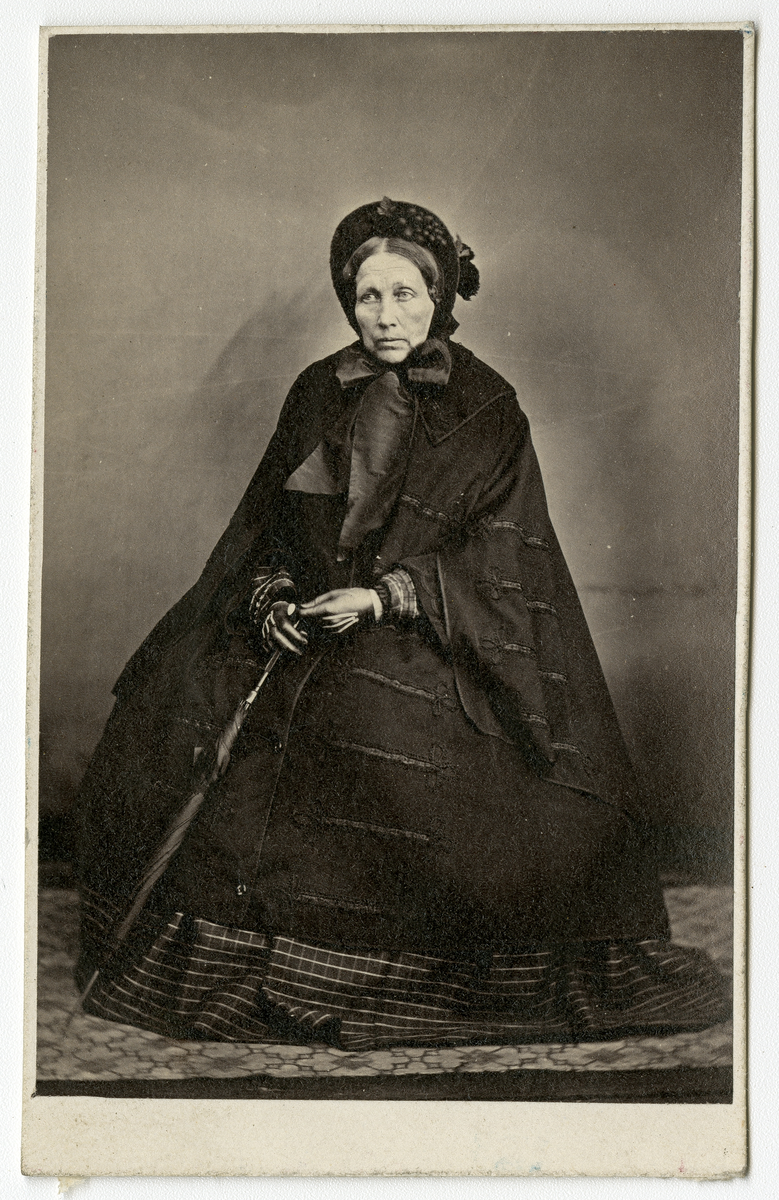 Portrettfoto av ukjent, eldre kvinne i mørke klær. Hun kan være kledd i sørgeklær
