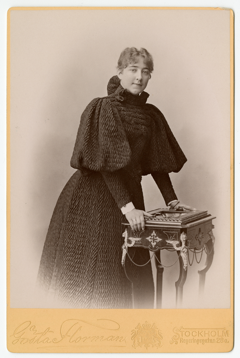 Kabinettkort foto av ukjent kvinne som lener seg over et bord, antagelig tatt på midten av 1890-tallet