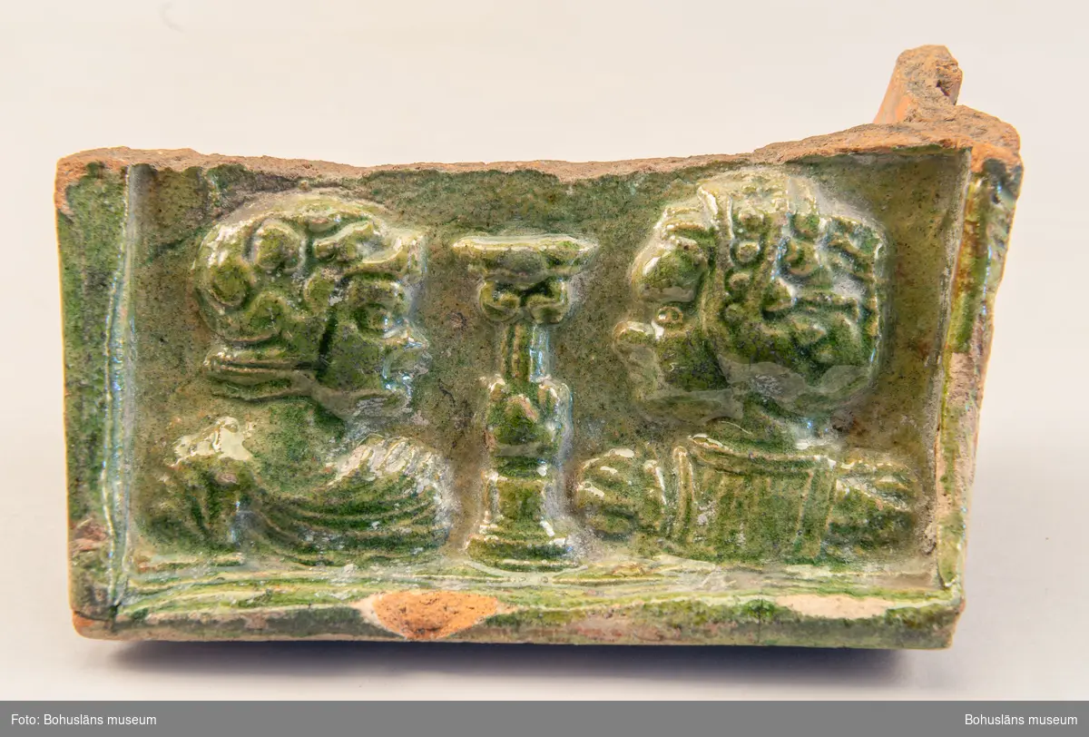 Kakel, skärvor från flera olika kakelugnar. Relieffdekor, grön och svartglaserat. En större frontbit bevarad med två människoansikten avbildade i profil, vända mot varandra (se foto).

Landskap: Bohuslän