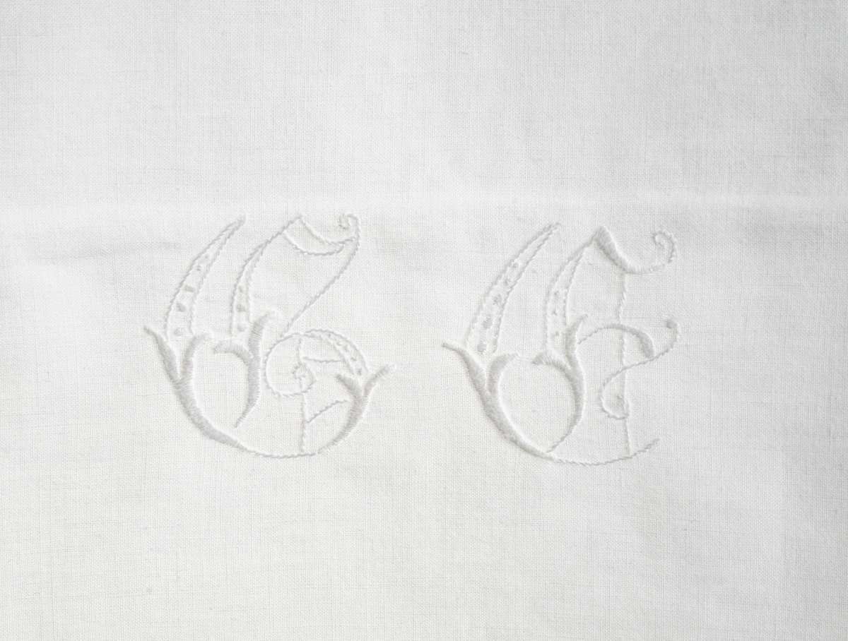 Pyntehåndkle i hvit bomull med monogram "G.E." i nedre kant og engelskbroderi m. hullsøm i den andre enden. Dobbel kant i begge kortender. Vevd i hel bredde.