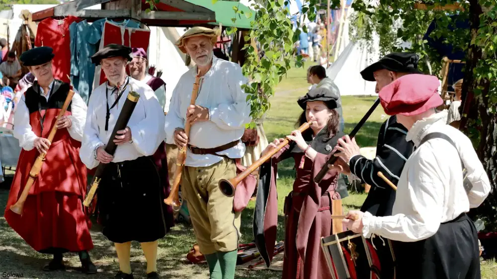 Et musikkensemble med fargerike drakter som spiller. Middelaldertelt i bakgrunnen