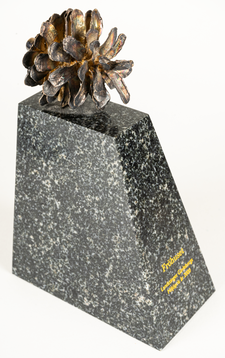 Skulptur "Fröhuset", av Gunnar Cyrén. Liten tallkotte i brons på fot av grön porfyr. Graverat i guld "Fröhuset Landstinget Gävleborg Miljöpris år 2000".