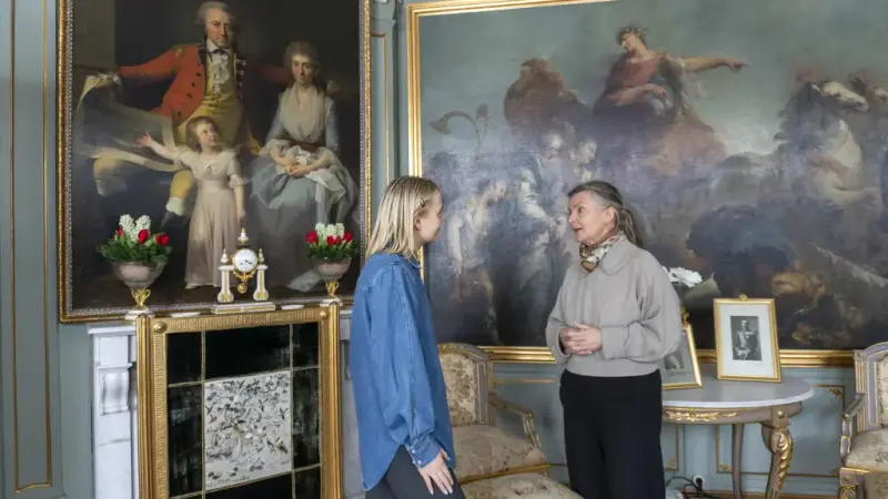 To damer snakker sammen foren noen store malerier. 