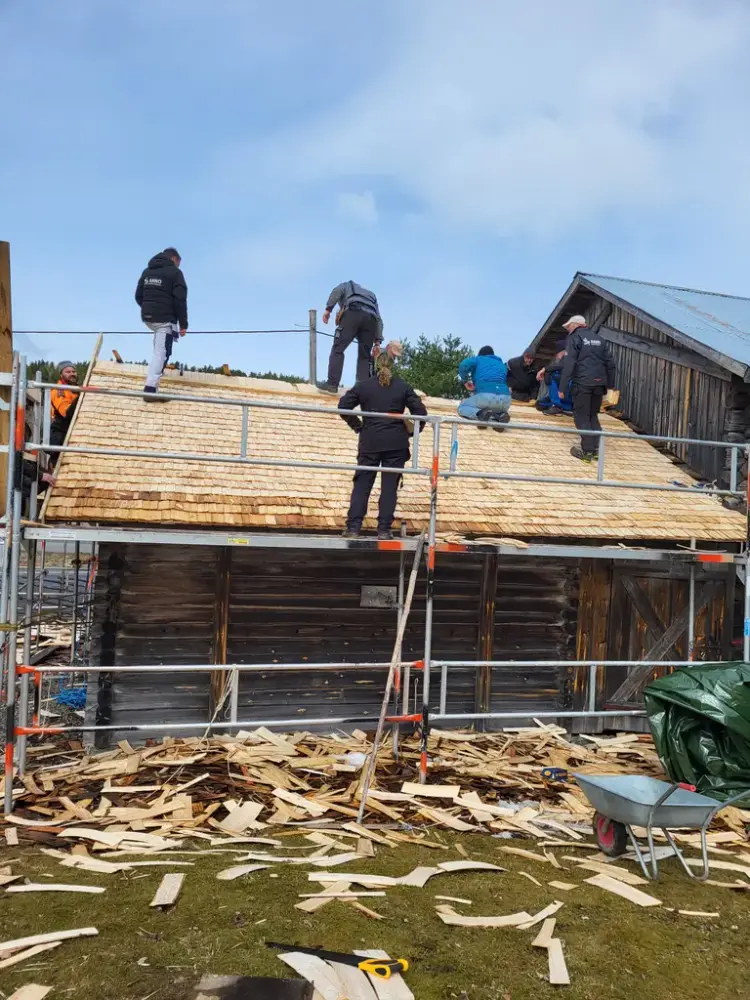 En gruppe håndverkere som legger nytt tak på en tømmerbygning.