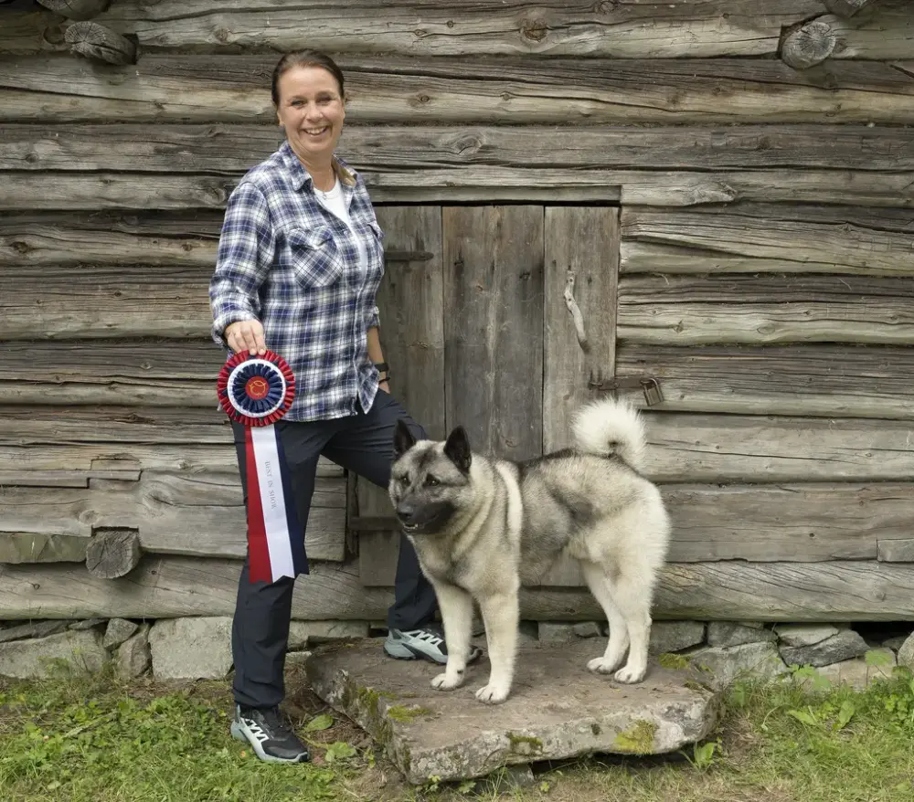 Dame med premie i hånden. Sammen med henne står en grå elghund 