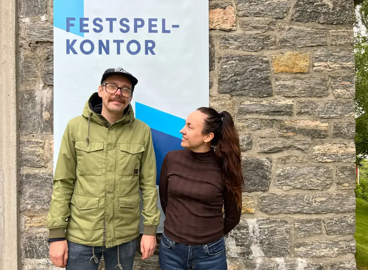 To personar framfor skilt med FESTSPELKONTOR Alternative text (no)