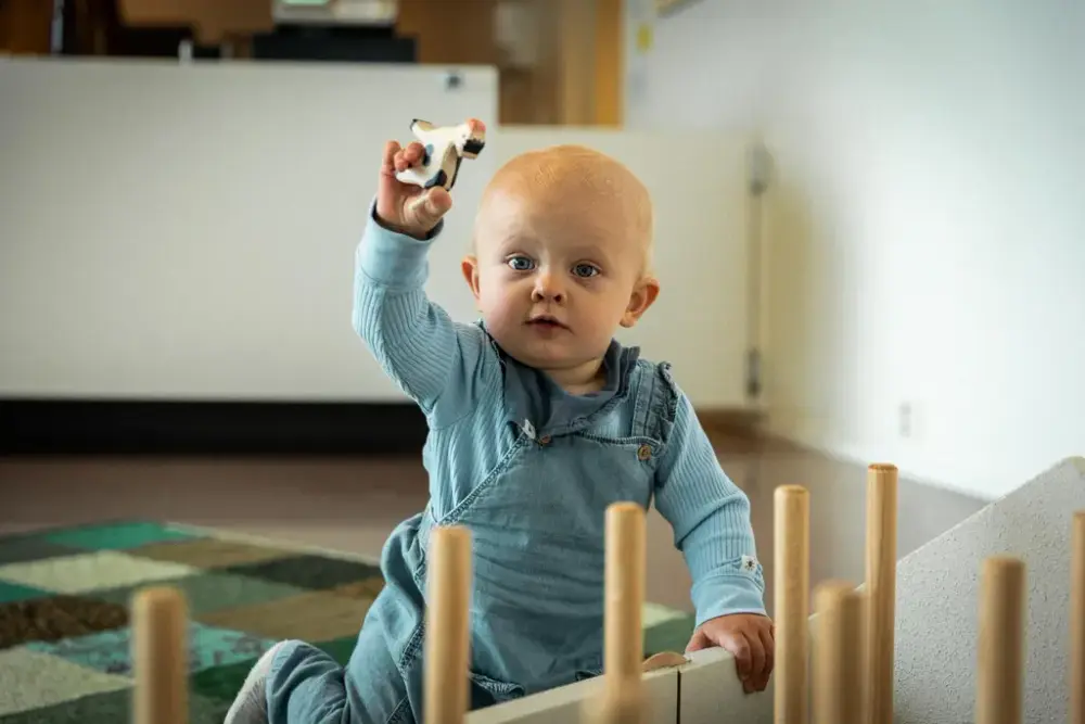 Barn på under ett år sitter ved langhusmodellen inne på museet og holder en lekeku laget av tre.