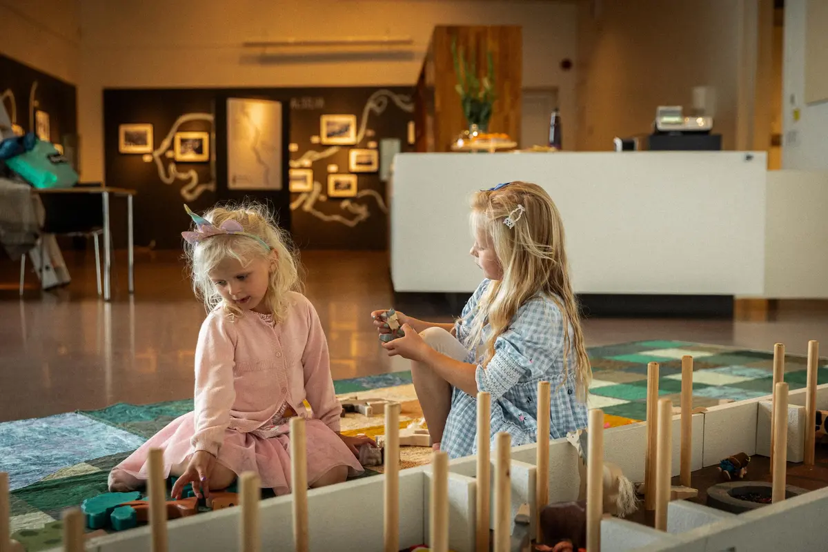 To barn sitter på gulvet og leker med langhusmodell inne på museet