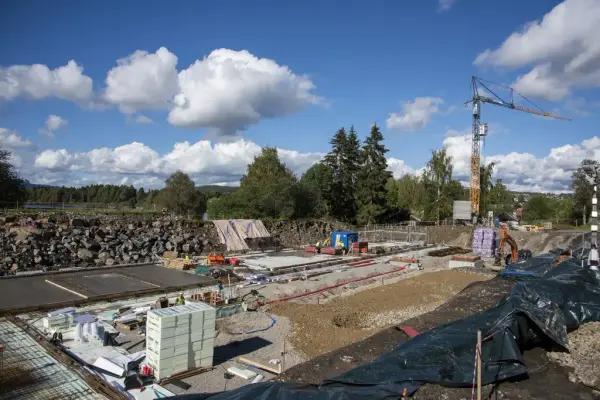 En del av grunnflata er støpt, noe mer er klargjort med markisolasjon og armeringsjern, og store stabler med mer isolasjonsplater står strategisk plassert mens byggekrana står i bakgrunnen.