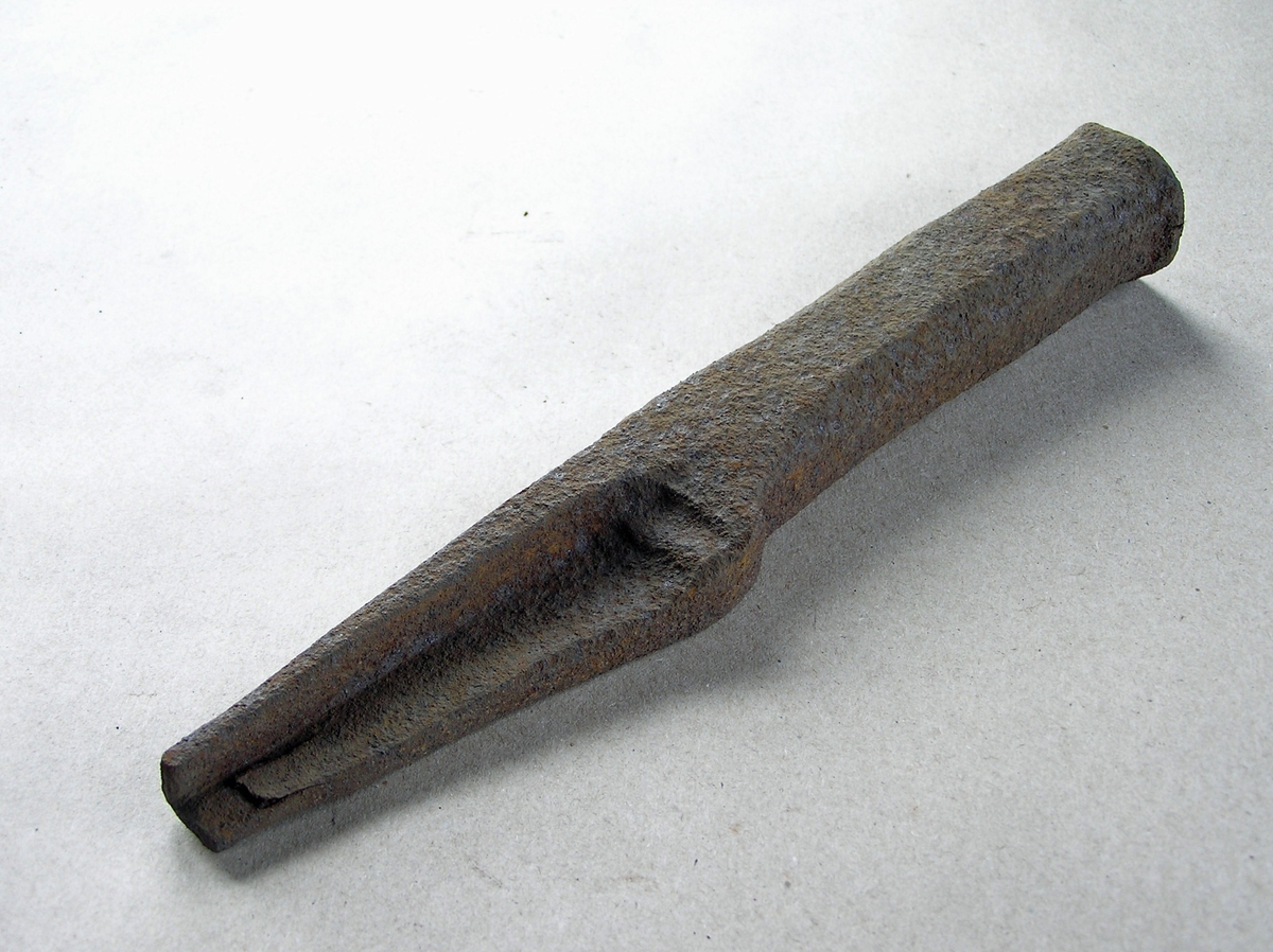 Smidd jernstykke til bruk ved smiing av merkeøks. Merket ble formet rundt stempelet. Stempeldel og håndtak i ett. L-formet stempel. Noe rust.