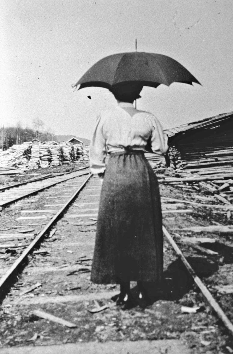 Fru Boeck (bakfra med paraply) ute i skinnegangen på sagbruket