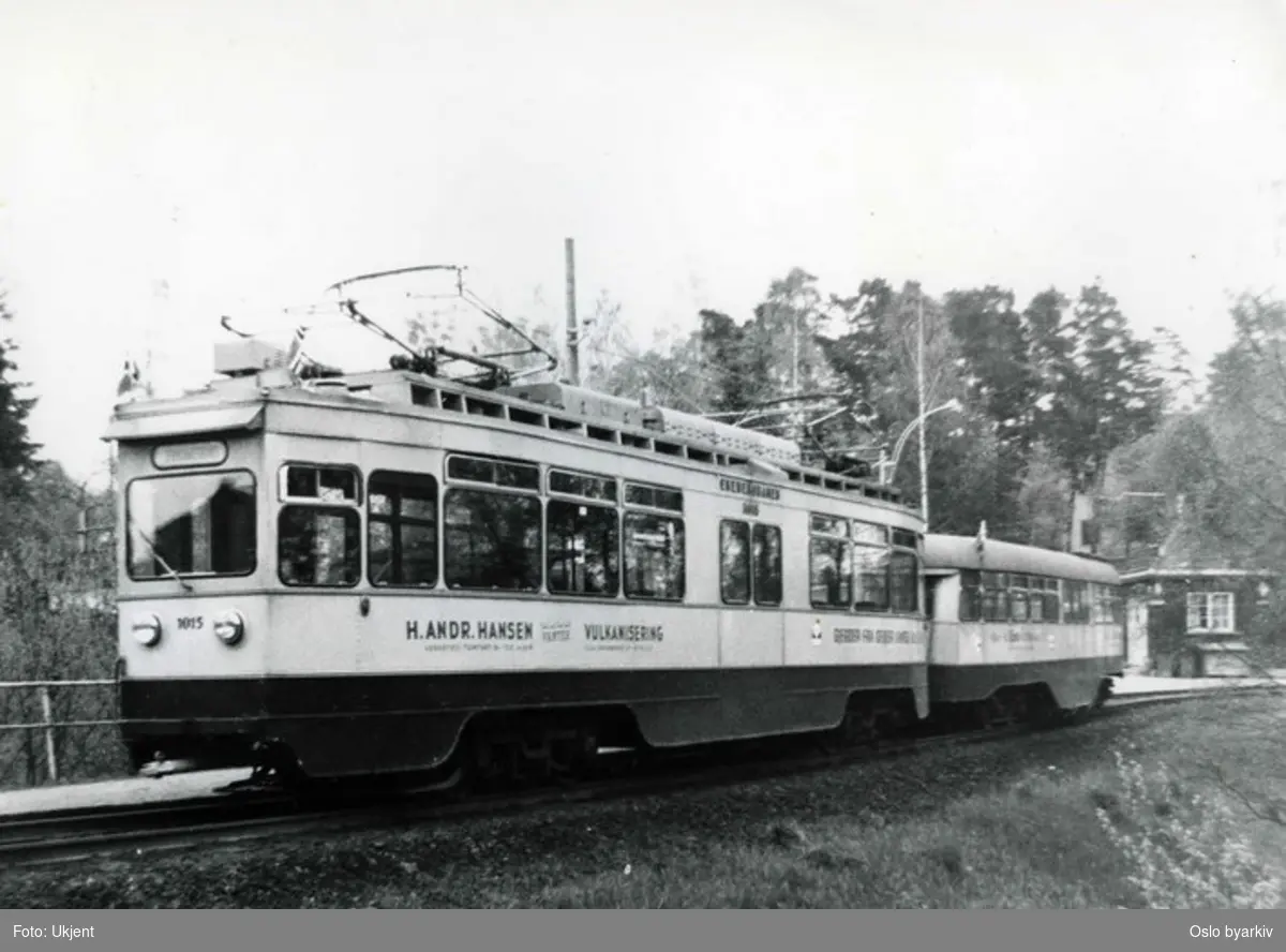 Trikk 1015 (i drift fra 1933 til 1974) med Skabo-tilhenger (kalt Olympiavogn) på Ekebergbanen. Ljabru endeholdeplass. Trikkereklame for H. Andr. Hansen verksted.