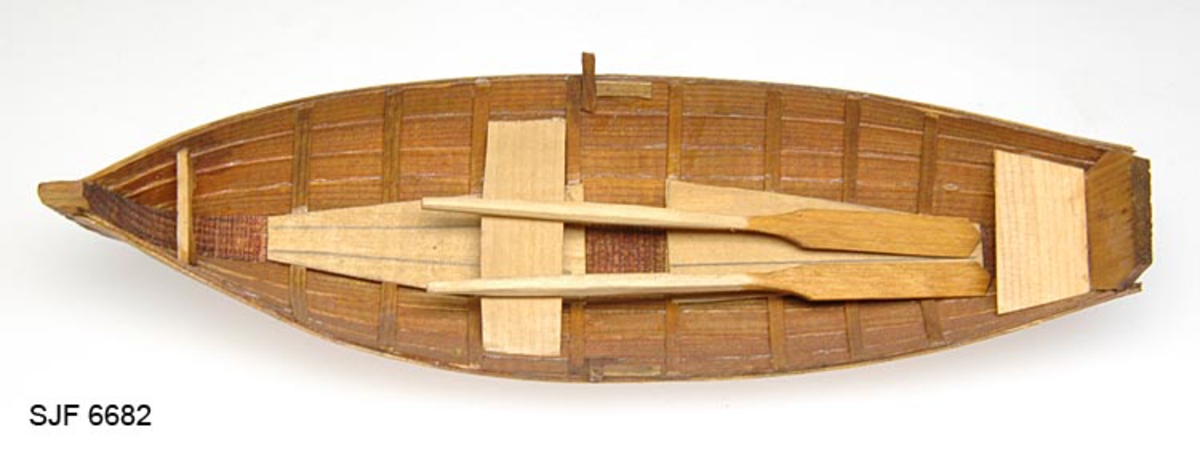 Modell av en "Fors-båt", det vil si en svensk fløterbåttype som var spesielt beregnet på bruk i fosser og stryk. Modellen er 22,9 centimeter lang og 6,8 centimeter bred. Den er sammenlimt av tynne furuspiler, som med unntak av tiljer og tofter, er brunbeisete. Båten har en tverr, skrått oppoverskrånende akterstavn. Tofta til roeren er plassert litt framfor båtens midtpunkt. I tillegg finnes det ei aktertofte for en passasjer. Med båten følger det et par 12,2 centimeter lange årer. Disse ser ut til å være lagd av gran.
