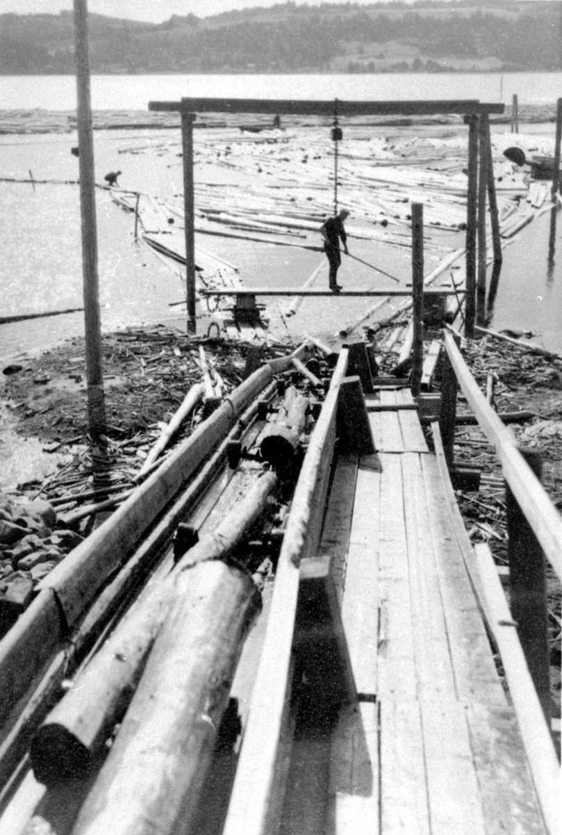 Arbeider drar tømmer opp kjerraten ved Strandsaga, Berger Langmoen A/S, Brumunddal.