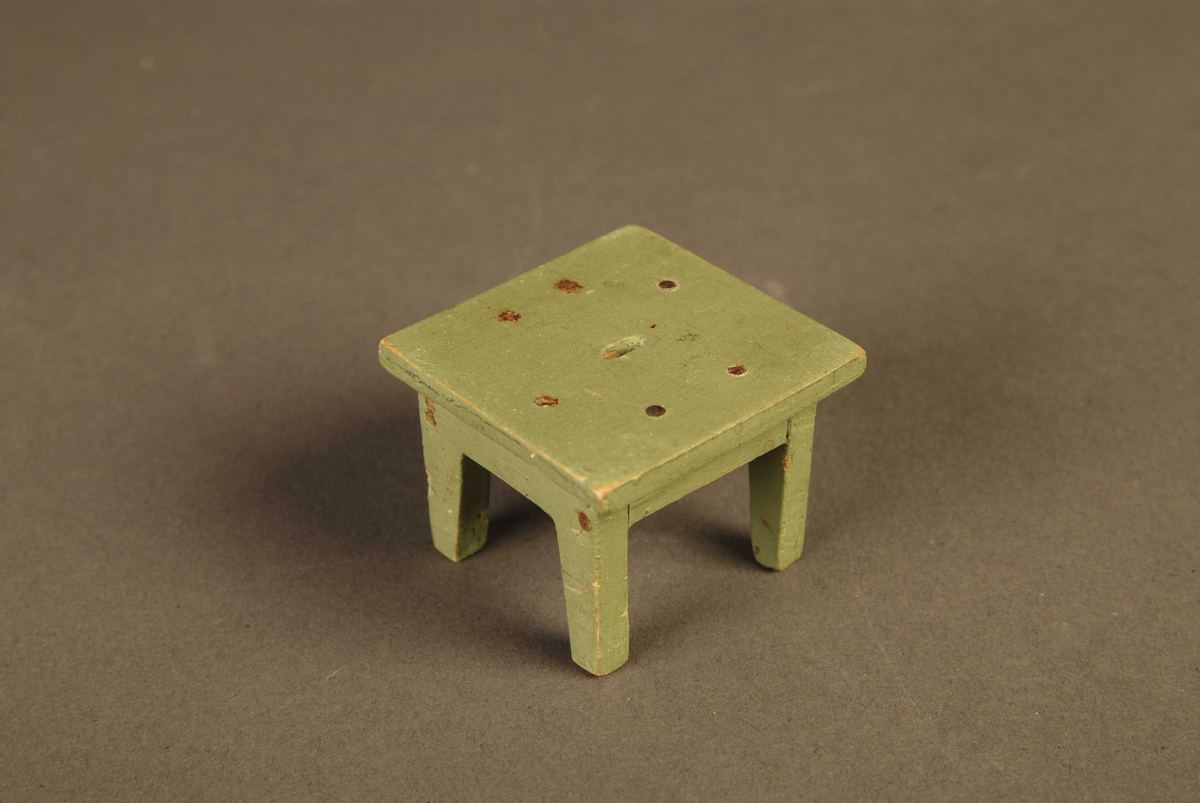 Tre identiske krakker laget av tre til dukkehus/dukkehusmøblement. De har kvadratiske seter med et ovalt hull på midten. Setet er dtiftet til en ramme med fire firkantede bein. Krakkene er malt grønn.