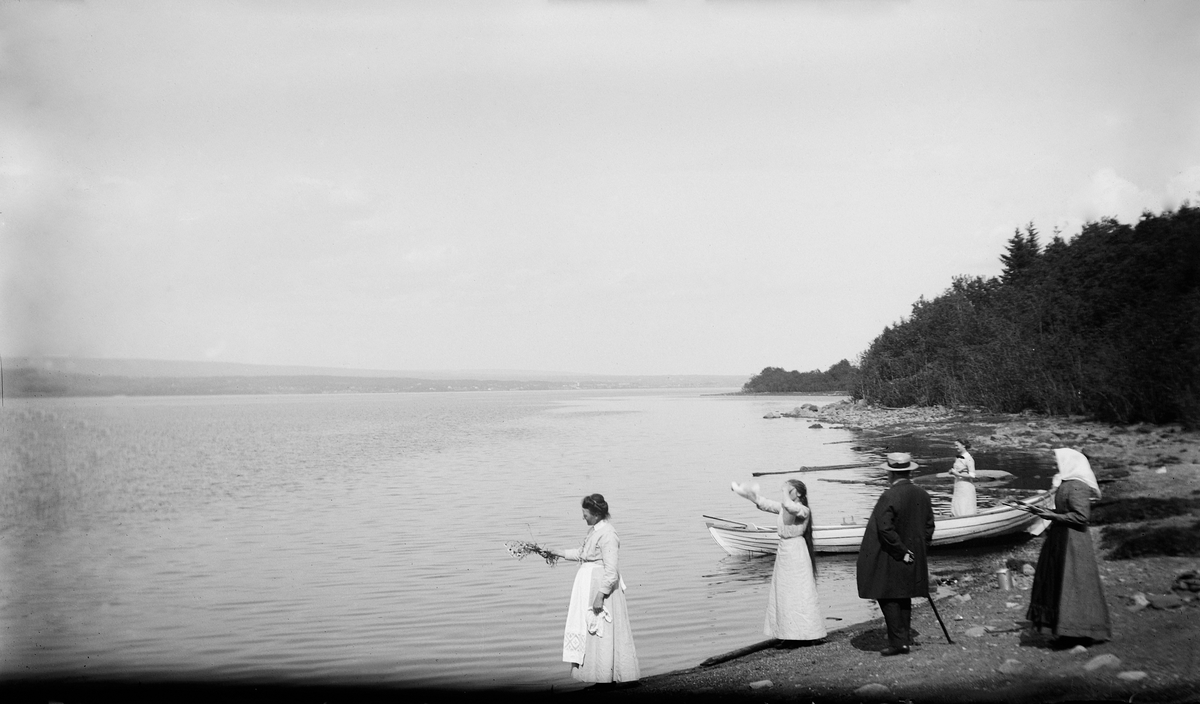 Fra venstre: Lovise Johannessen, ukjent, Olaus Johannessen, Aagot (Morbech) Johannessen, dame med skaut, strandkanten ved Mjøsa nær Atlungstad i Stange. Robåt.