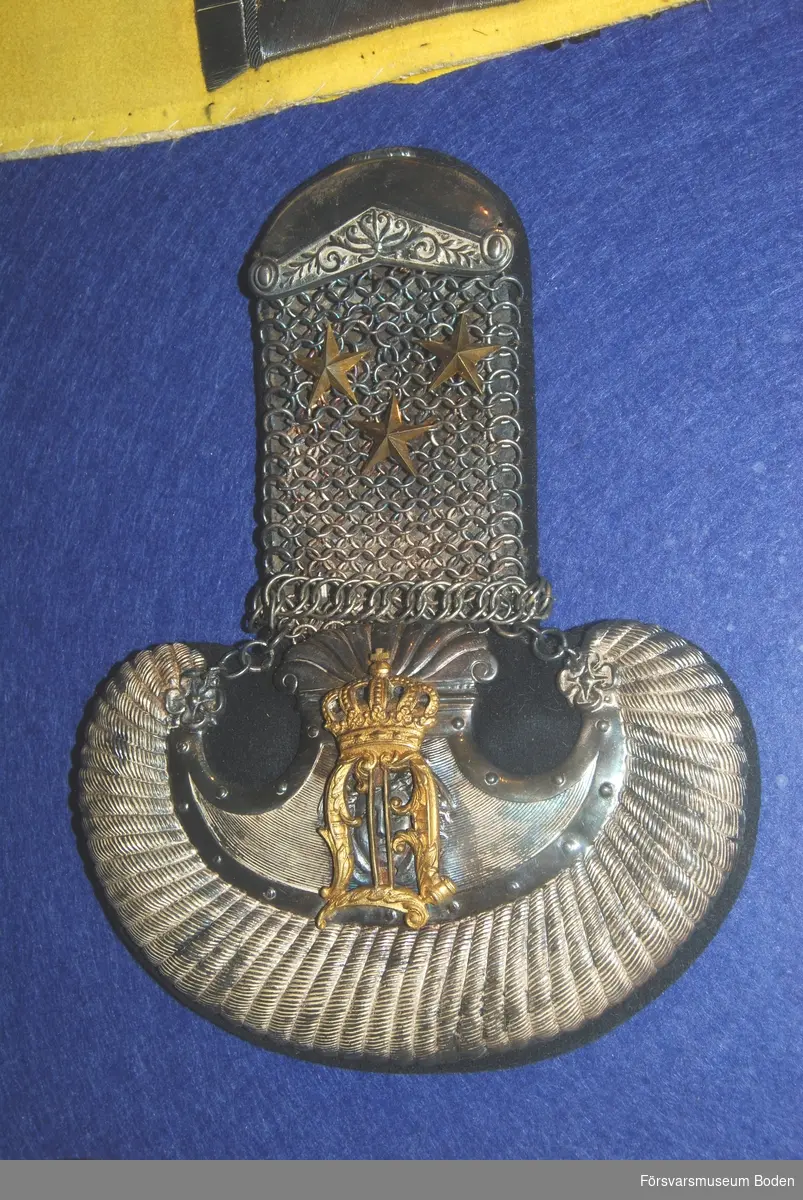 1 par epåletter av silver med matta av mörkblått kläde. Med Oscar II:s kungliga namnchiffer i guld samt tre stjärnor betecknande kapten.