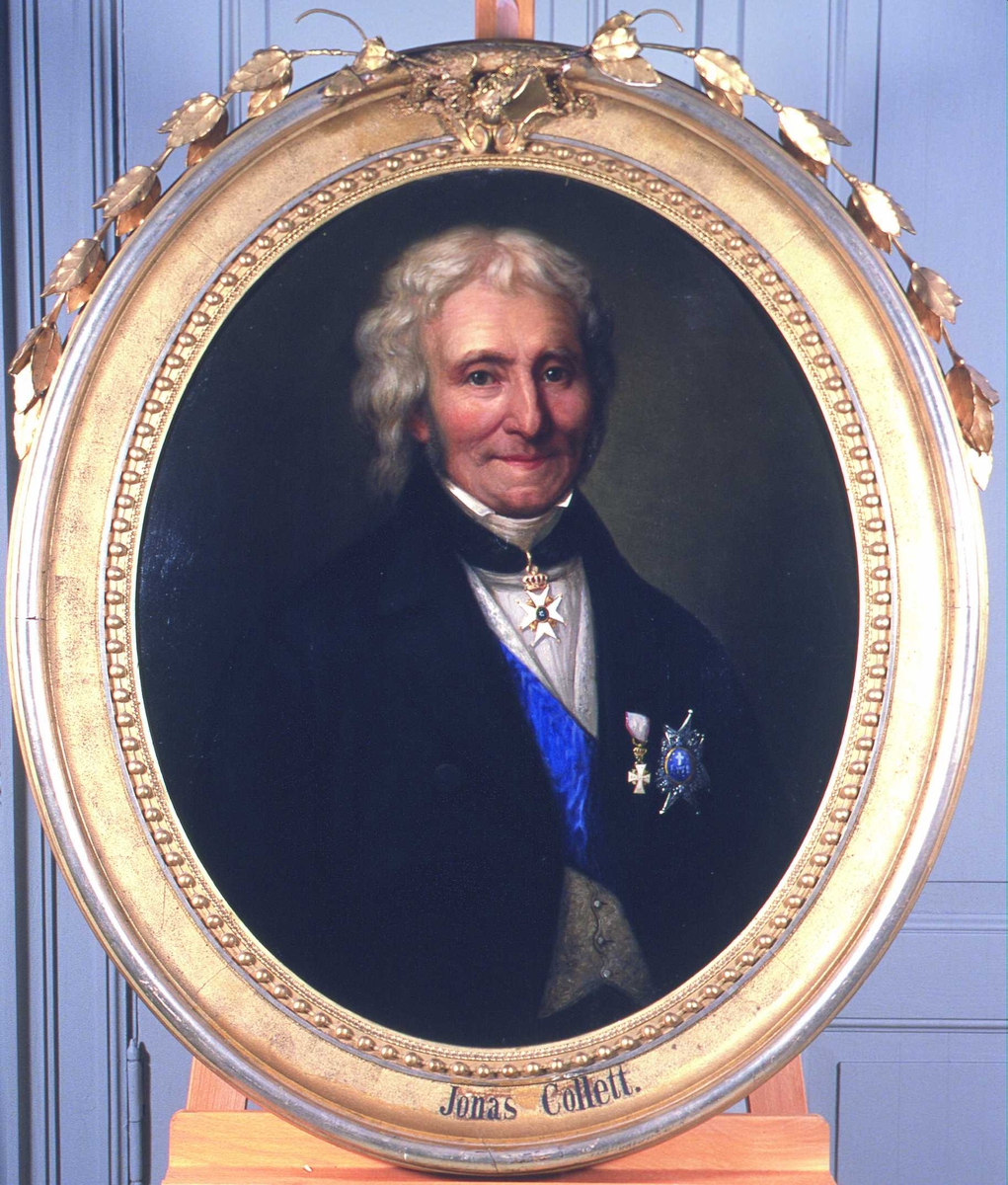 Portrett av statsråd Jonas Collett Grått hår, krøllet.  Mørk kjol (jakke), grå vest, blått ordensbånd m/3 ordener. 