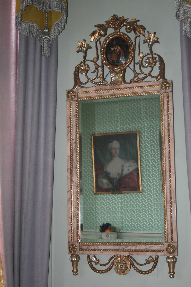 Rektangulært speil med innfatning av rød marmor. Toppstykke med medaljong m/bilde, laubærkrans, drueklaser.