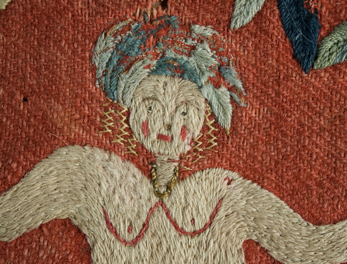 Rød putetrekk  av ull med brodert dekor, bakside i hvitt skinn og mellomstoff av grovt linne.