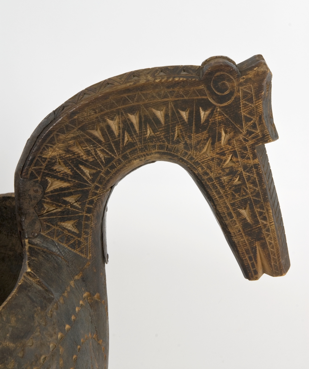 Symmetrisk kjenge med hestehode på hver side. Skåret ornamentikk i form av geometriske mønster på hodene og rundt kanten på utsiden.