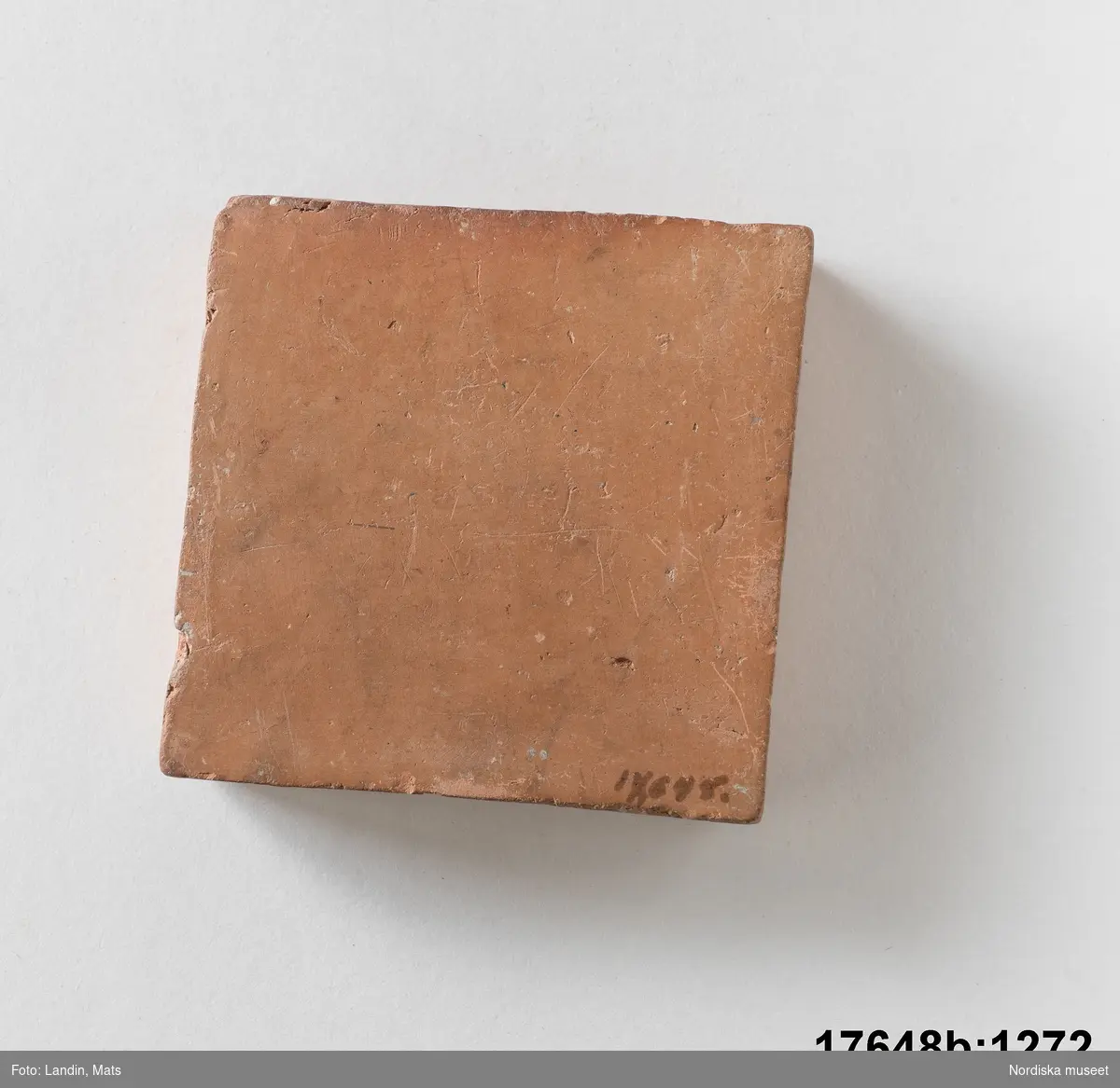 Kvadratisk platta av bränd oglaserad röd lera. På en sida text: "Bränd men oglaserad".
/Leif Wallin 2014-01-07