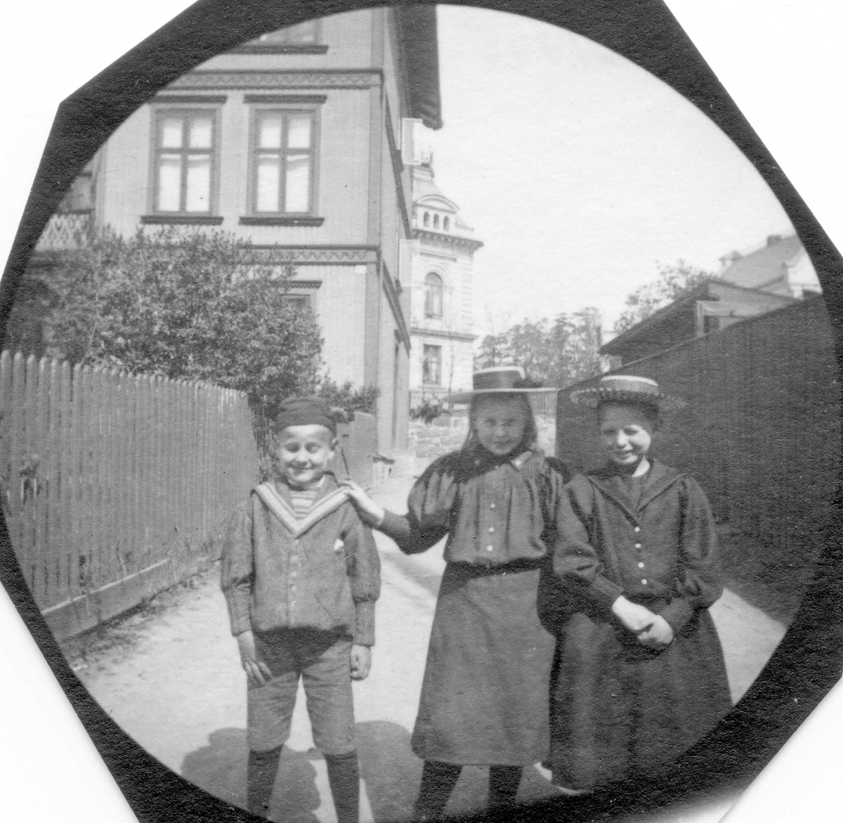 To jenter og en gutt i boliggate, Vestheimgaten, Oslo, med gjerde, hage og stort trehus. Betty  Reimers i midten.