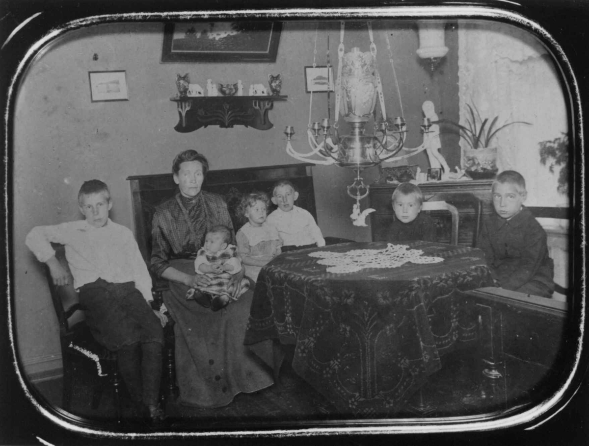 Stueinteriør med kvinne og 6 barn, Stoler, sofa, bord, kommode, gardiner. Vogtsgt., Oslo, ant. 1911