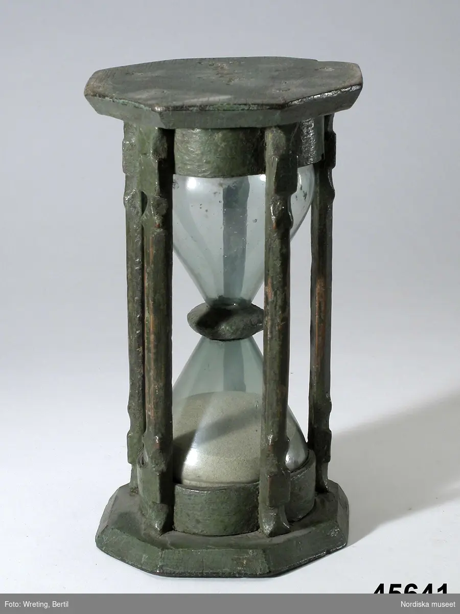 Timglas, sandur, med ställning av skuret och grönmålat trä. Under bottnen skuren inskrift: "anno 1694".
/Anna Arfvidsson Womack 2022