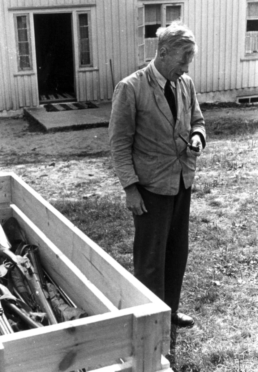 Knut Vatnestrøm står foran et hus ved en kasse med geværer. Frostemyr 1941.