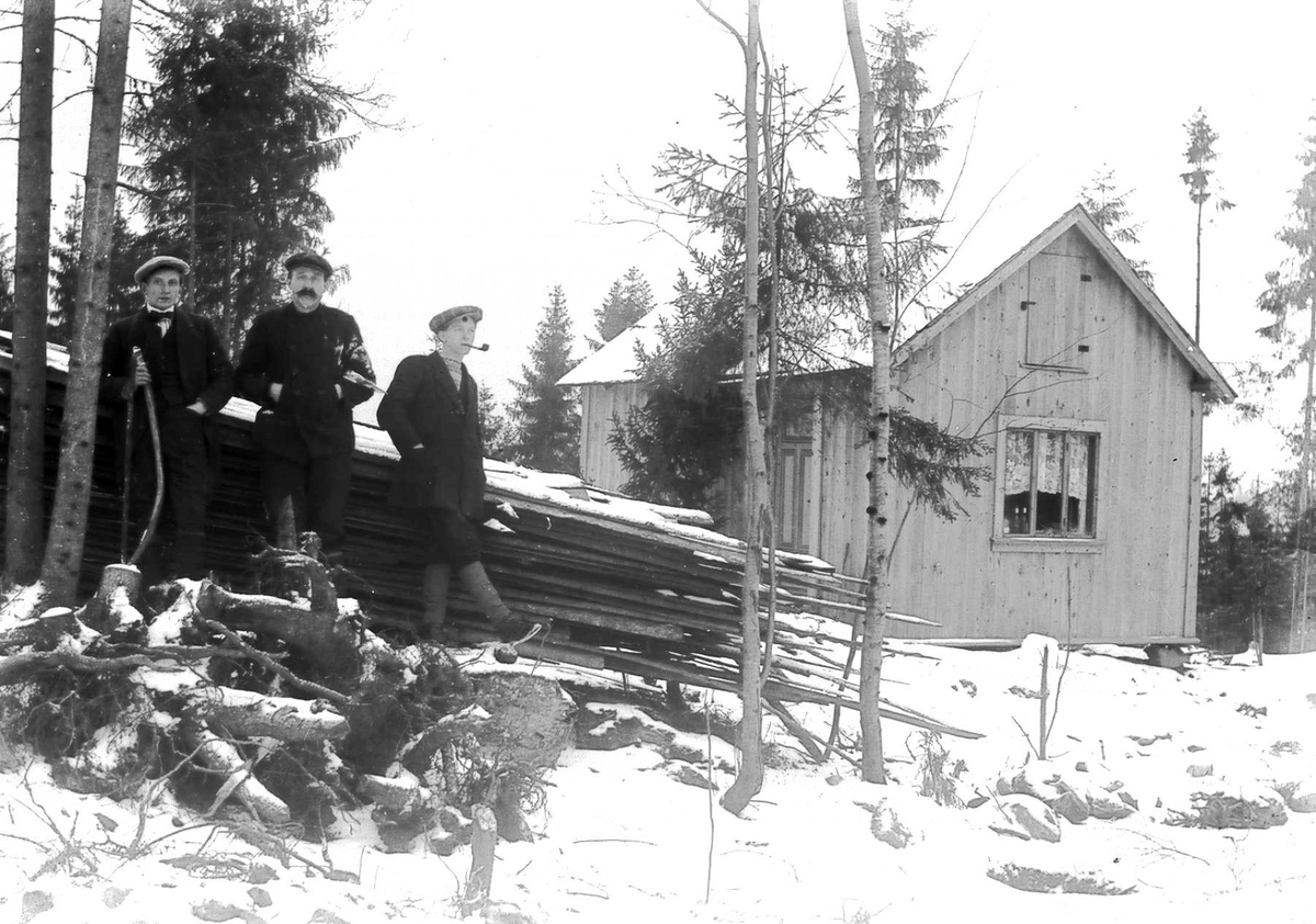 Tre menn stående utenfor sommerhuset i Ringstabekkveien vinterstid. Hytta er fotografert fra kjøkkensiden