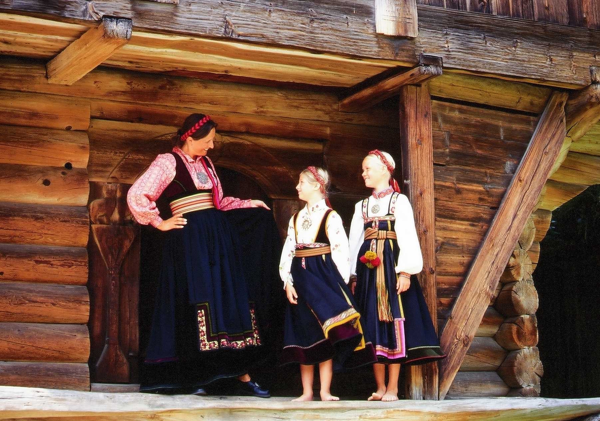 Kvinne og to jenter i telemarksbunad foran loftet fra Søndre Tveito,
bygning nr. 133 i Telemarkstunet på Norsk Folkemuseum.