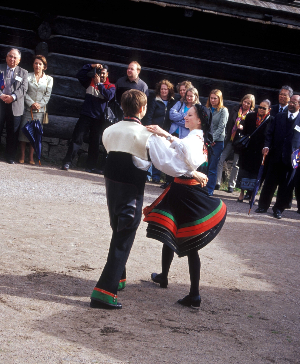 Norsk Folkemuseums dansegruppe, kledd i setesdalsdrakter, danser folkedans i Numedalstunet på Norsk Folkemuseum. Et par danser  i forgrunnen mens publikum ser på.