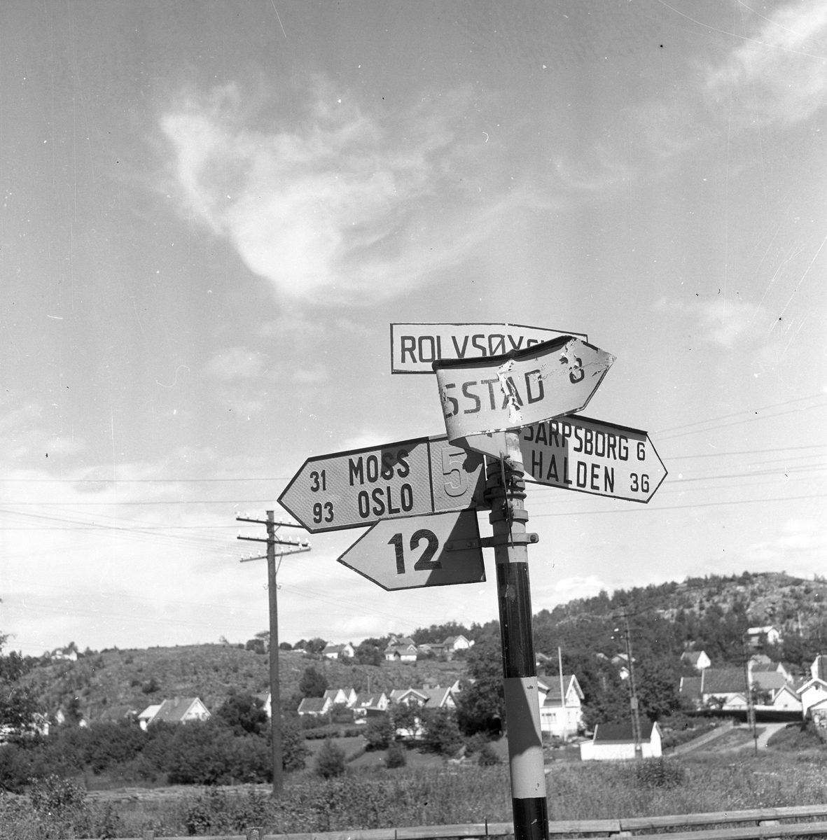 Langs Riksvei 1står det et trafikkskilt ved Rolvsøy som henviser til Moss, Sarpsborg, Halden etc. Fotografert 7. juli 1958.