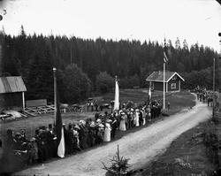 Oppstilt, festkledd folkemengde ved vei med flagg og faner, 