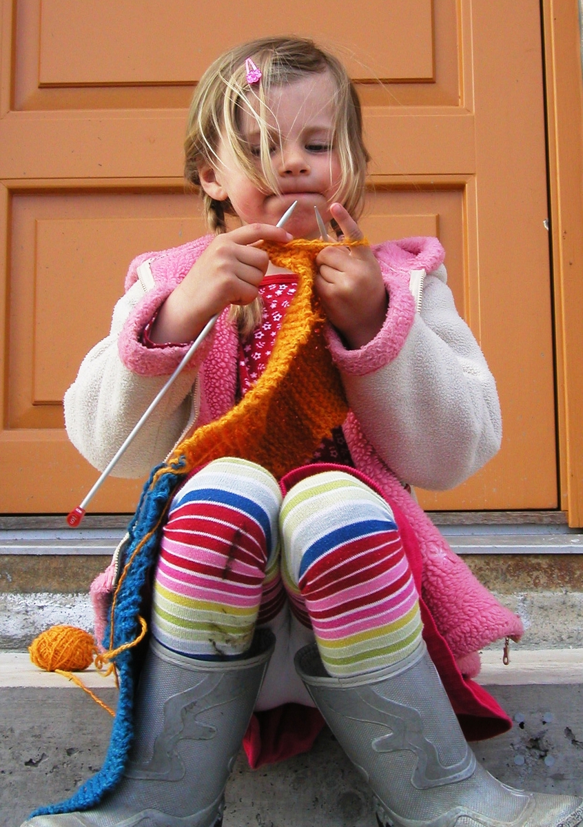 Fem år gamle Margit med sitt første strikketøy - et skjerf hun skal gi til sin farfar i bursdagsgave. Fotografert utenfor familiens hjem på Lille Tøyen Hageby i 2004.
