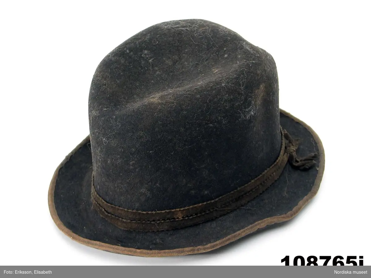 Hel mansdräkt bestående av 12 delar.
a. skjorta
b. rock av svart kläde
c. väst av svart kläde
d. knäbyxor av sämskskinn
e. förskinn
f. 1 par strumpor vita
g. handskar av sämsskinn
h. 1 par skor
i. hatt
j. hatt
k. långhalsduk
l. löskrage.
/BEEL

a. Mått: längd: 96 cm. Längd: 52 cm - ärmlängd. Vidd: 52 cm - ärmvidd
Material: Textil, linne. Lingarn - broderier, band. Teknik: Handvävning. Gåsögon. Trådbundet broderi. Broderi - plattsöm. Handsömnad
Rak mansskjorta i handvävt hellinnetyg, vävt i gåsögon.  Båltyget i ett stycke, sidosömmar med 13 cm långa sidosprund. Öppning fram, 31 cm långt sprund. Rektangulärt halsspjäll,  rynkningar mot 8,5 cm hög krage med broderier på både in- och utsida i kanten, plattsöm och trädsöm, nuggor i katnen. Två fastsydda mönstervävda knytband, blå/vit och vit. Vidsydd ärm med ärmspjäll. Rynkningar mot 1,3 cm bred ärmlinning broderad med plattsöm och trädsöm, nuggor i kanten,  mönstervävda knytband.. Skjortan är handsydd.
/Inga-Lill Eliasson 2007-04-17


f. 1 par strumpor  skaftlängd 40 cm, fot 26 cm; tvåändsstickade av vitt ullgarn i slätstickning.
g.
h.
i.
j.Hatt, svart rundkullig filthatt, kullens höjd 14 cm, brätte bredd 5 cm; lätt uppböjt brätte kantat med bomullsband, delvis fodrad med ljust bomullstyg.
/BEEL
k.Längd: 139 cm. Bredd: 18,5 cm. Material: Halvlinne. Telnik: Handvävning, dräll. Handsömnad.
Långhalsduk vävd i dräll, avlång,  randigt mönster av ca 1,3 cm breda ränder i dräll med tuskaft emellan. Handsydd smal fållad kant.
Anm: Något gulnad.
/INEL
l. Löskrage "hassdutj" längd 34 cm, bredd 8,7 cm, rak remsa av vit fin linnelärft, broderi i plattsöm längs långsidorna med små "nuggor" i kanten. Baksida av en bit linneväv med ränder i kypertvariation, knytband i ändarna av mönstervävt linneband i ljusgrått och vitt.

Berit Eldvik maj 2006