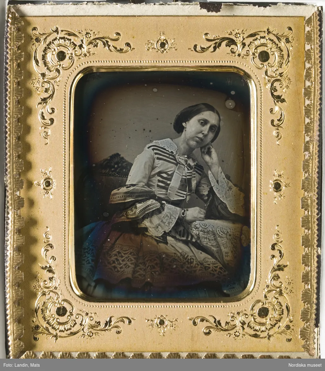 Porträtt, knäbild av prinsessan Eugénie (1830–1889), sittande. Mittbenat, slätt, uppsatt hår, iklädd mönstrad klänning med vid kjol, vit krage och ärmar med volang. Dagerrotyp / daguerreotyp i glasad ram. Passepartout av papp med gulddekoration i nyrokokostil. Nordiska museet inv.nr 121931
-
Portrait of Princess Eugénie of Sweden and Norway (1830–1889). Ninth-plate daguerreotype.