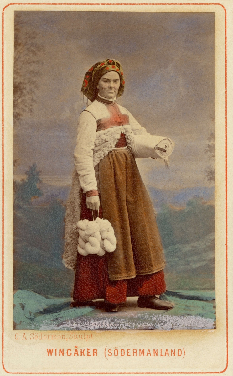 Kvinna i sockendräkt från Vingåker, Södermanland. Dräktdocka med huvud skulpterat av C A Söderman, visad på världsutställningen i Wien 1873. Handkolorerat fotografi.