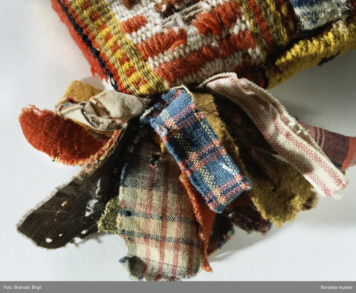 Folkkonst. Kuddhörn med bandtofs tillverkad av överblivna bitar av vadmalstyg. Föremål ur Nordiska museets samlingar.