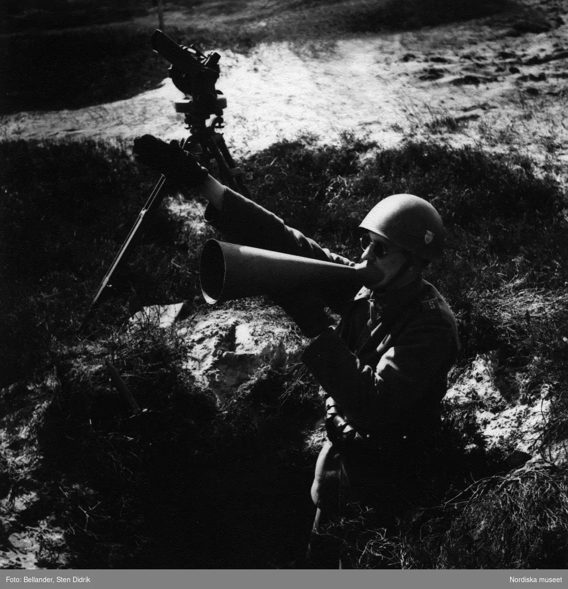 Soldat står i skyttegrop och ropar i en lur.